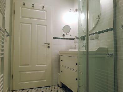 Blick ins Badezimmer der Ferienwohnung mit Tür, Waschbeckenschrank und Runddusche im Vordergrund.