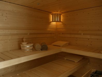 Ein Blick in die Sauna der Ferienwohnung Rhein-Lahn-Glück. Auf der oberen Saunaliege stehen ein Holzzuber mit Schöpfkelle, daneben liegen zwei gerollte Handtücher.