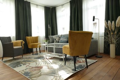 Gesamtansicht des Wohnzimmers der Mittelrhein-Ferienwohnung mit zwei gelben Sesseln, Korbstuhl, Schlafsofa, und Glastisch