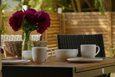 Gedeckter Tisch auf der Terrasse der Ferienwohnung mit Geschirr, Blumen und Brotkorb.