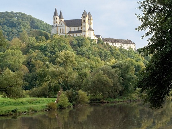 Das Kloster Arnstein liegt ragt hoch über der Lahn aus Bäumen hervor.