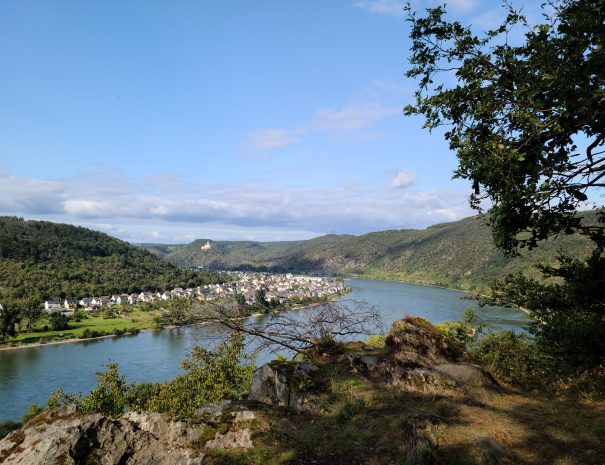 Im Vordergrund ist ein felsiger Platz zu sehen, im Hintergrund das Mittelrheintal mit Spay und der Marksburg.