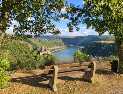 Blick auf Burg Katz und die Loreley, im Vordergrund steht eine Aussichtsbank im Abendlicht